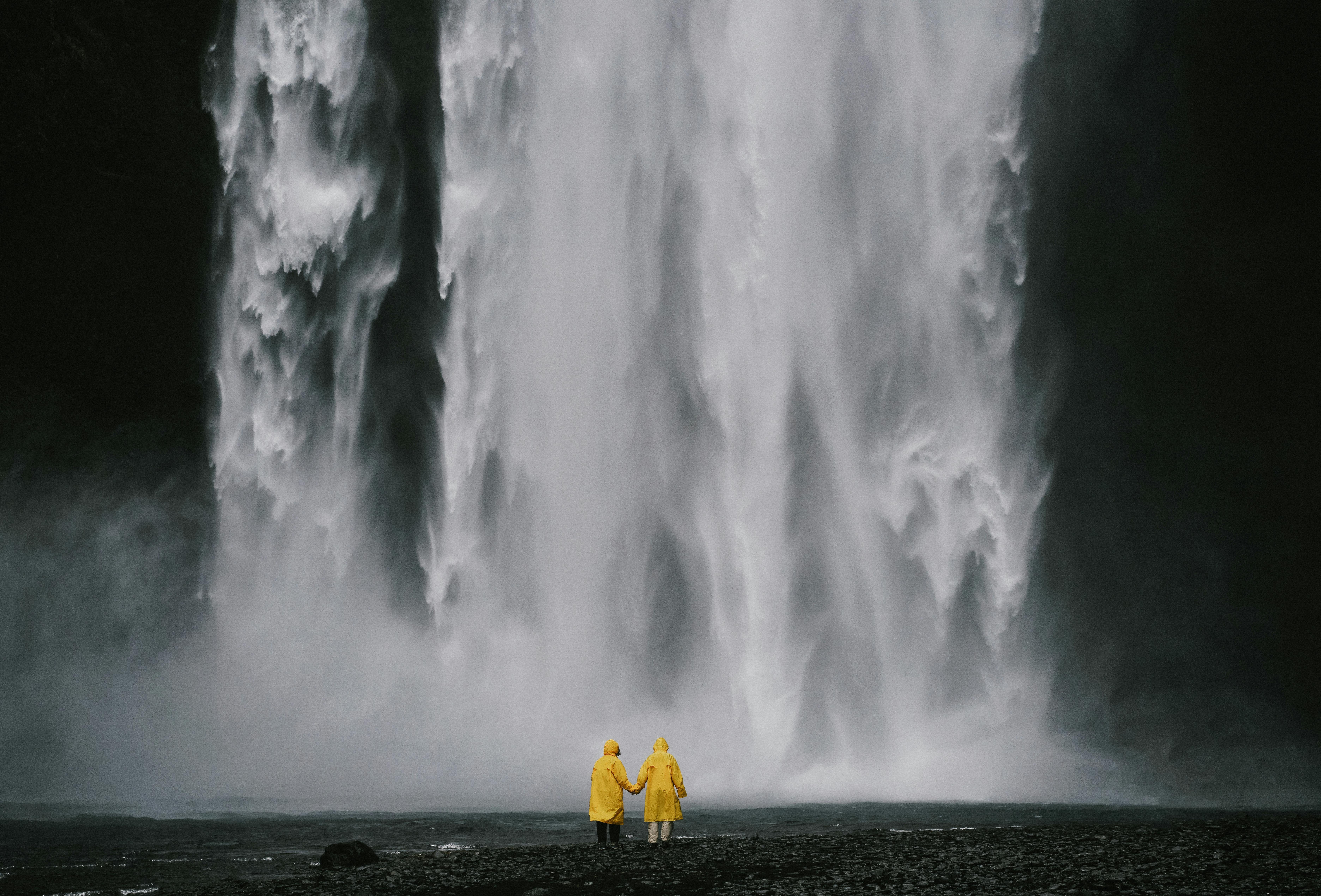 Massive waterfall with two small figures in yellow raincoats at its base